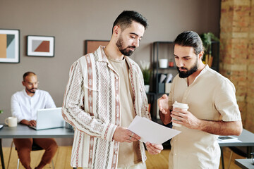Young confident businessman showing his colleague or ceo financial paper and discussing information...