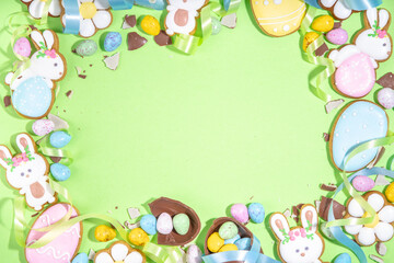 Happy Easter colorful flatlay. Colorful sugared and chocolate Easter eggs, sugar glazed cookies with festive holiday ribbon on light green background top view copy space