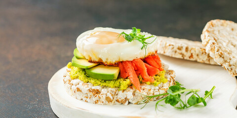 Crispbread with avocado, egg and a salmon against a dark background. Healthy breakfast. Selective focus. Copy space