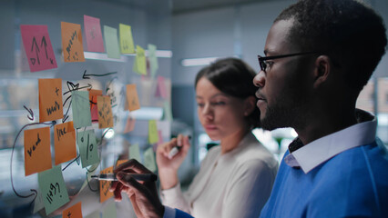 Side view of African-America colleagues discuss and write on glass board in modern office