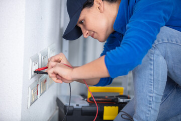 young brunette woman repairs an electric socket with a multimeter