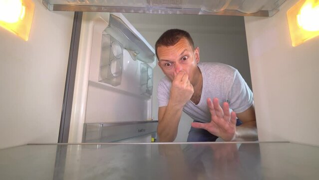 young white European opens refrigerator to wash it. Wearing gloves, with a sponge and spray from sniffing and plugging the nose with your hand because of the terrible smell. Germs and freon leakage.
