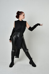 Full length portrait of pretty red haired female model wearing black futuristic scifi leather costume. Dynamic standing poses with gestural hands on a white studio background.