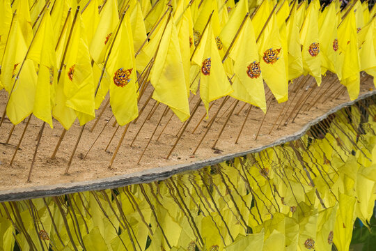Yellow prayer flags stuck in sand over reflecting water at a wat temple.