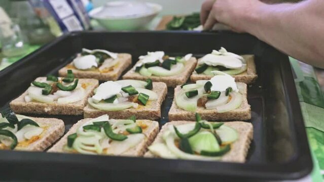 Making toasts on a baking tray with green spicy jalapeno pepper, white onion and mozzarella cheese. Adding ingredient to the sandwiches for baking.
