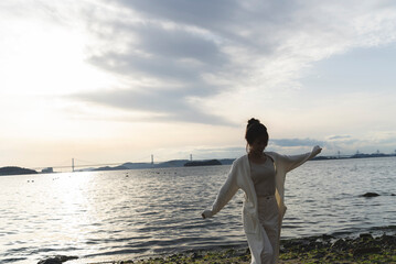 Fototapeta premium 夕暮れの海岸線を歩く女性