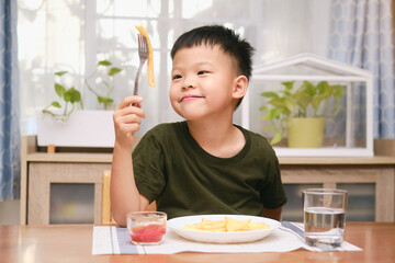Cute happy smiling Asian 5 yers old kindergarten boy child using fork eating French fries potato...
