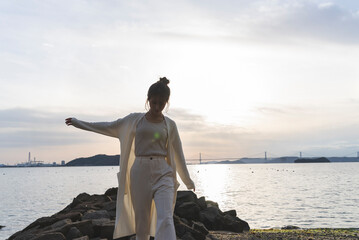 夕暮れの海岸線を歩く女性