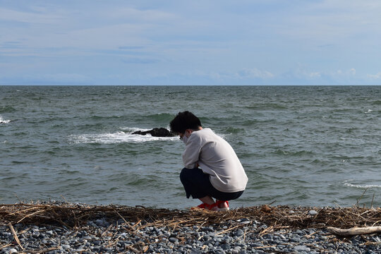 A man squatting and waiting for driftwood on the shore full of twigs on the beach where driftwood flows