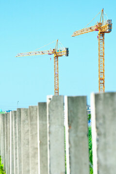 Two construction cranes above a row of concrete pillars