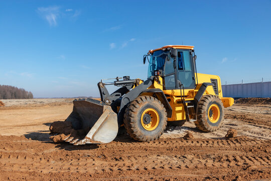 Bulldozer or loader moves the earth at the construction site against the blue sky. An earthmoving machine is leveling the site. Construction heavy equipment for earthworks.
