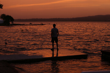 Man looking towards horizon by lake at sunset