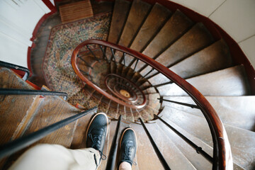 Man in stylish black boots staying on wooden spiral staircase. Selective focus on male's shoes. Stairway in old residential building in Paris, France. Copy space.