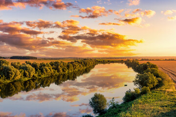 A sunset or sunrise scene over a lake or river with cloudy skies reflecting in the water on a summer evening or morning.