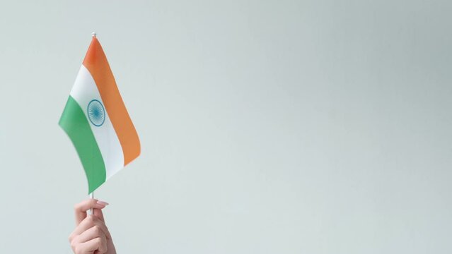 India flag. National symbol. Embassy consulate. Female hand waving tricolor with saffron orange white green horizontal stripes isolated on light neutral copy space background.