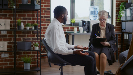 African american man talking about alcohol addiction at aa therapy meeting with people. Person having conversation with woman therapist and patients at rehabilitation program session.