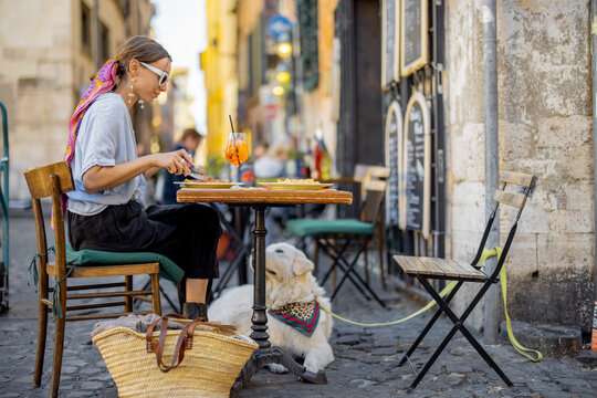 Woman eating italian pasta while sitting with a dog at restaurant on the street in Rome. Concept of Italian gastronomy and travel. Maremma, italian shepherd dog