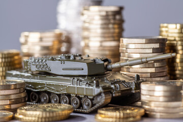 Tank between stacks of coins as a symbol of high armament expenditure - obrazy, fototapety, plakaty