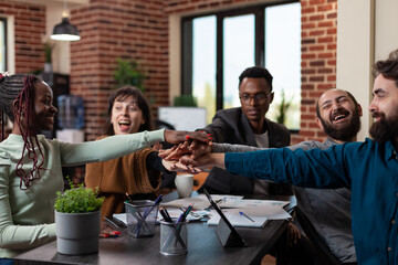 Excited successful multiracial businesspeople putting hand on hand enjoying business achievements during marketing meeting in startup office. Diverse team working at company turnover