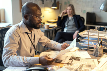 Young serious male detective looking through criminal profiles and picking up data about suspects...