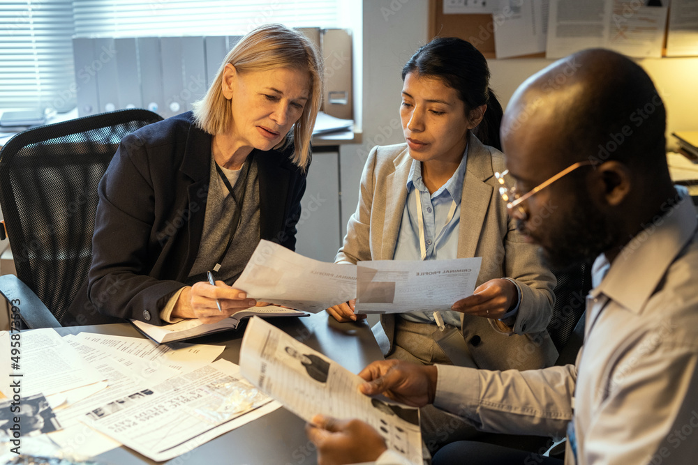 Aufkleber two intercultural female agents comparing information in criminal profiles while discussing personal