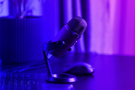 laptop, smartphone, microphone on a black table. Home studio podcast interior. Microphone, laptop on the table. Online live radio studio desk with microphone in the foreground, entertainment concept