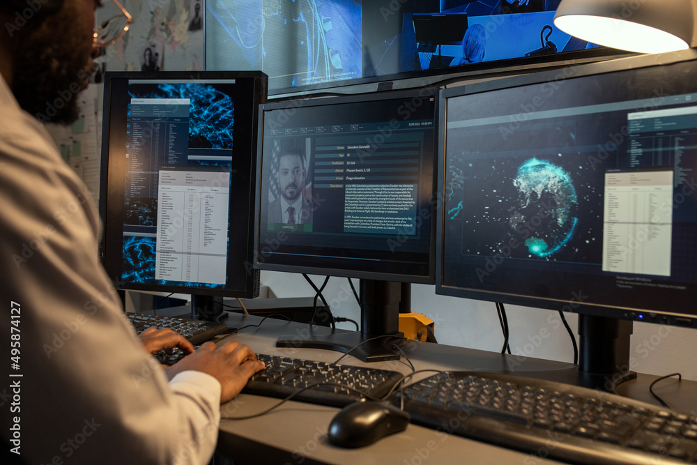 Aufkleber Young policeman entering personal data of suspect into computer database while sitting in front of monitors in office