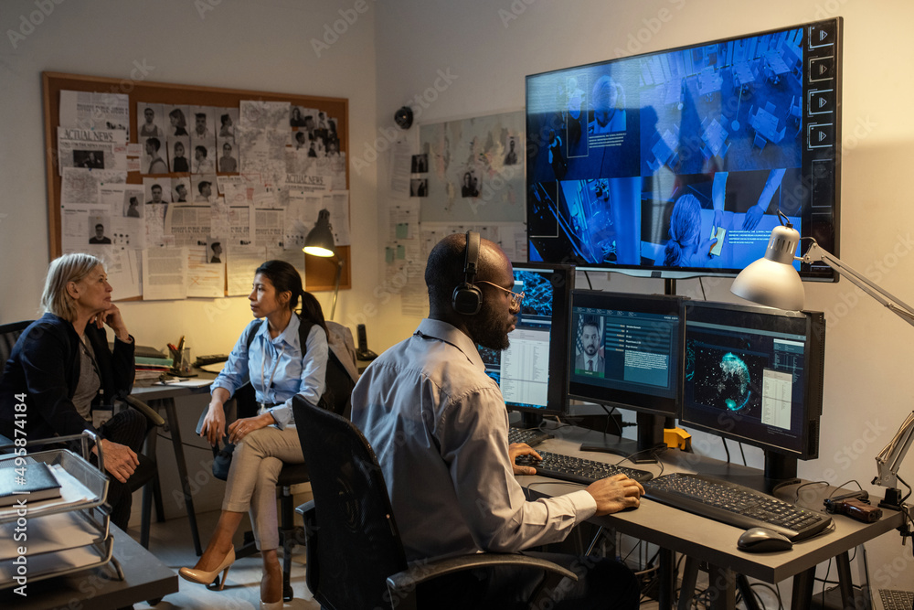 Aufkleber young african american fbi agent sitting in front of computer monitors and screen in office while wa