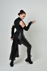 Full length portrait of pretty red haired female model wearing black futuristic scifi leather...