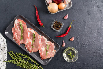 raw pork steaks ready to cook iso spices and rosemary sprigs on a dark ceramic tray and black...