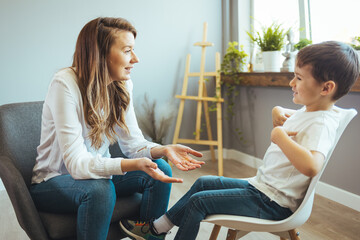 Cheerful young kid talking with helpful child counselor during psychotherapy session in children mental health center. Child counselor during psychotherapy session - obrazy, fototapety, plakaty