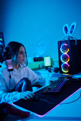 Happy woman putting on headphones and playing computer game. Female gamer in glasses sitting and looking at computer monitor. © Евгений Вершинин