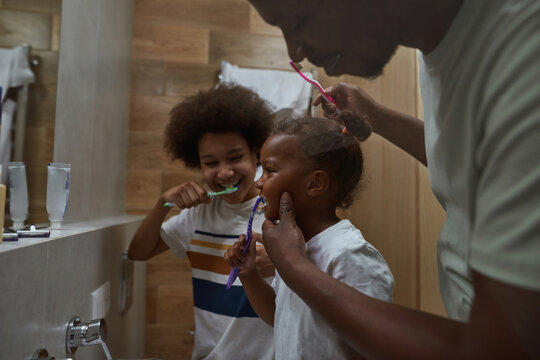 Father teaching daughter brushing teeth near son