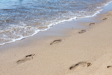 Footprints of a man on the yellow beach sand from walking barefoot by the sea with water that washes away the footprints.
