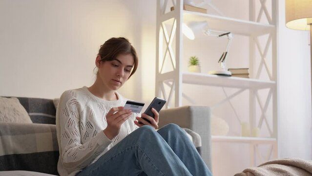 Online payment. Internet order. Gadget shopping. Cheerful satisfied woman buying store purchase on phone with credit card at home living room.