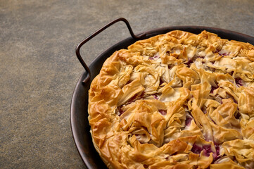 Homemade cherry pie or tart from filo dough on on metal tray on wooden background. Top view. Close up