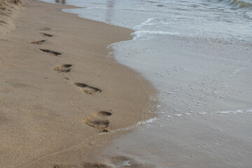 Footprints in the sand beach. Footprints in the sand against a sea wave. Footprints on a sunny day with golden sand, beach, wave and footsteps