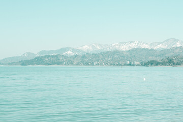 Calm blue sea wallpaper with snowy mountain peaks at a distance. Fresh spring background in blue colors. 