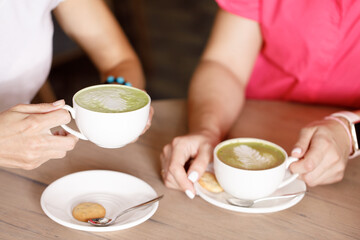two girl friends in a cafe drink matcha, tea, coffee, cappuccino 