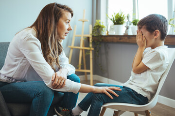 Psychologist touching shoulder of frustrated little boy while trying to help him. Young supported...