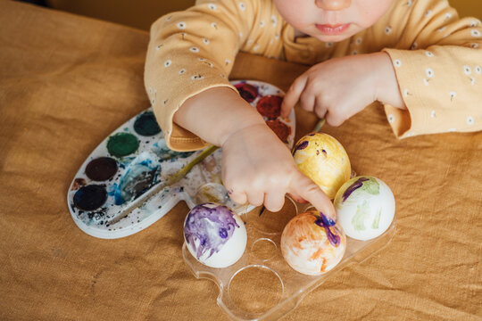 A Child Paints easter eggs on the yellow background.
