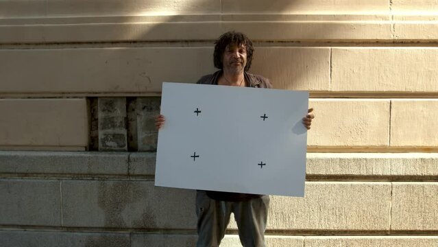 Portrait of old homeless person standing outdoors holding a empty placard. Homeless man with blank billboard.