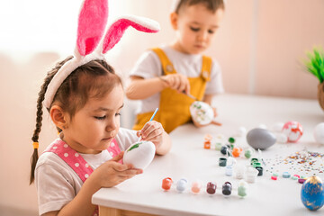 Obraz na płótnie Canvas A little girl of Asian appearance and a boy of European appearance draw Easter eggs. Easter concept. Preparation for Easter. Happy Easter.