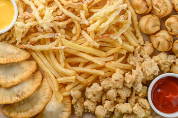 Close-up fragment of a multiple french fries potato chips and fried pies as a food backdrop composition