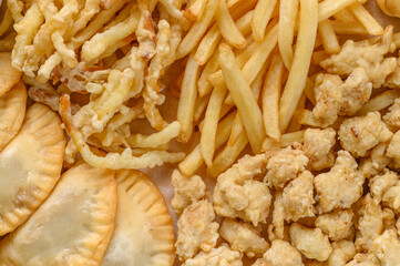 Close-up fragment of a multiple french fries potato chips and fried pies as a food backdrop composition