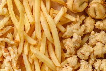 Close-up fragment of a multiple french fries potato chips and fried pies as a food backdrop composition