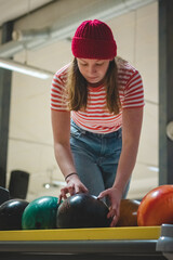 Fototapeta premium young amateur female bowler wearing a red cap and a spotted t-shirt takes the correct weight ideal ball and prepares internally for her throw. Concentration