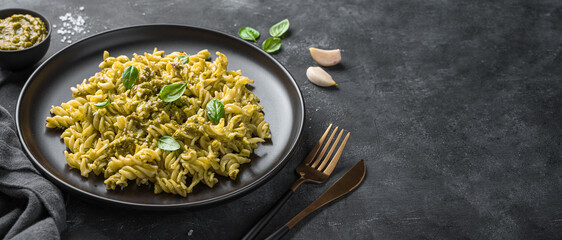 Fusili pasta with pesto sauce, fresh basil leaves and sesame seeds on a dark background. Side view, copy space.