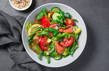 Fresh salad with salmon, avocado, cucumber and tomatoes on a dark background. Healthy food. Top view.
