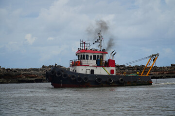 Old tug boat with black exhaust plume in the harbor of the Brazilian port city of Recife, state of Pernambuco, Brazil.